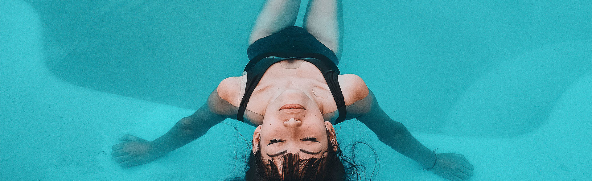 Junge Frau mit schwarzem Badeanzug sitzt in einem Pool.